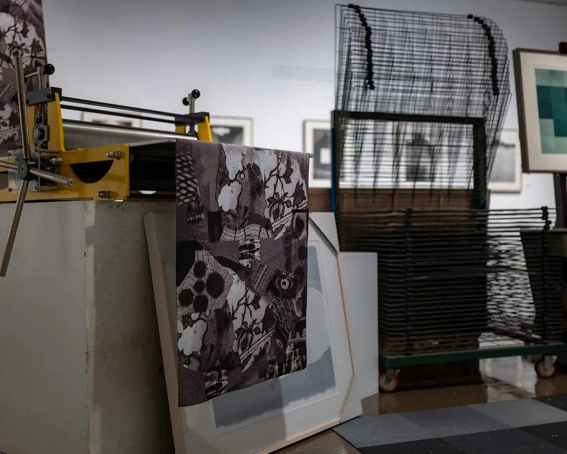 Tórculo de un taller de grabado con una estampa recién tirada sobre la platina y un secadero metálico con pruebas al fondo